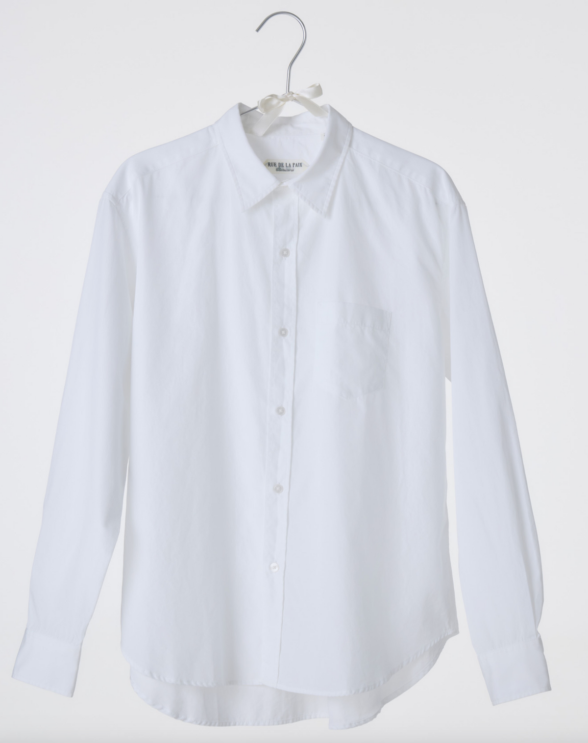 Rue de la Paix La Garçonne Shirt in white on a hanger, with a classic collar, button front, chest pocket and curved hem
